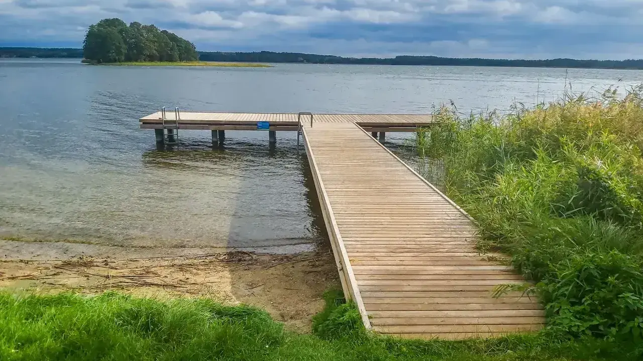 Drewniany pomost na jeziorze, z którego roztacza się widok na wyspę. Może to być miejsce, gdzie pobierana jest opłata za pomost na jeziorze.