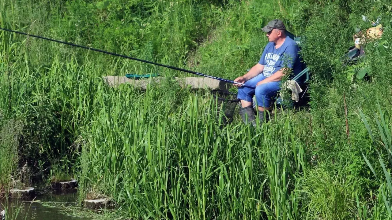 Mężczyzna łowi ryby nad turkusowym jeziorem w Koninie, otoczony bujną zielenią.