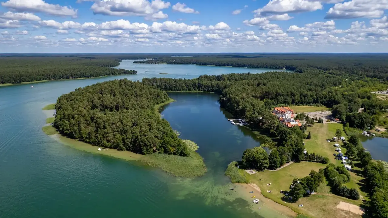 Malownicze jezioro Lechickie otoczone lasem, z hotelem i polem kempingowym na brzegu.