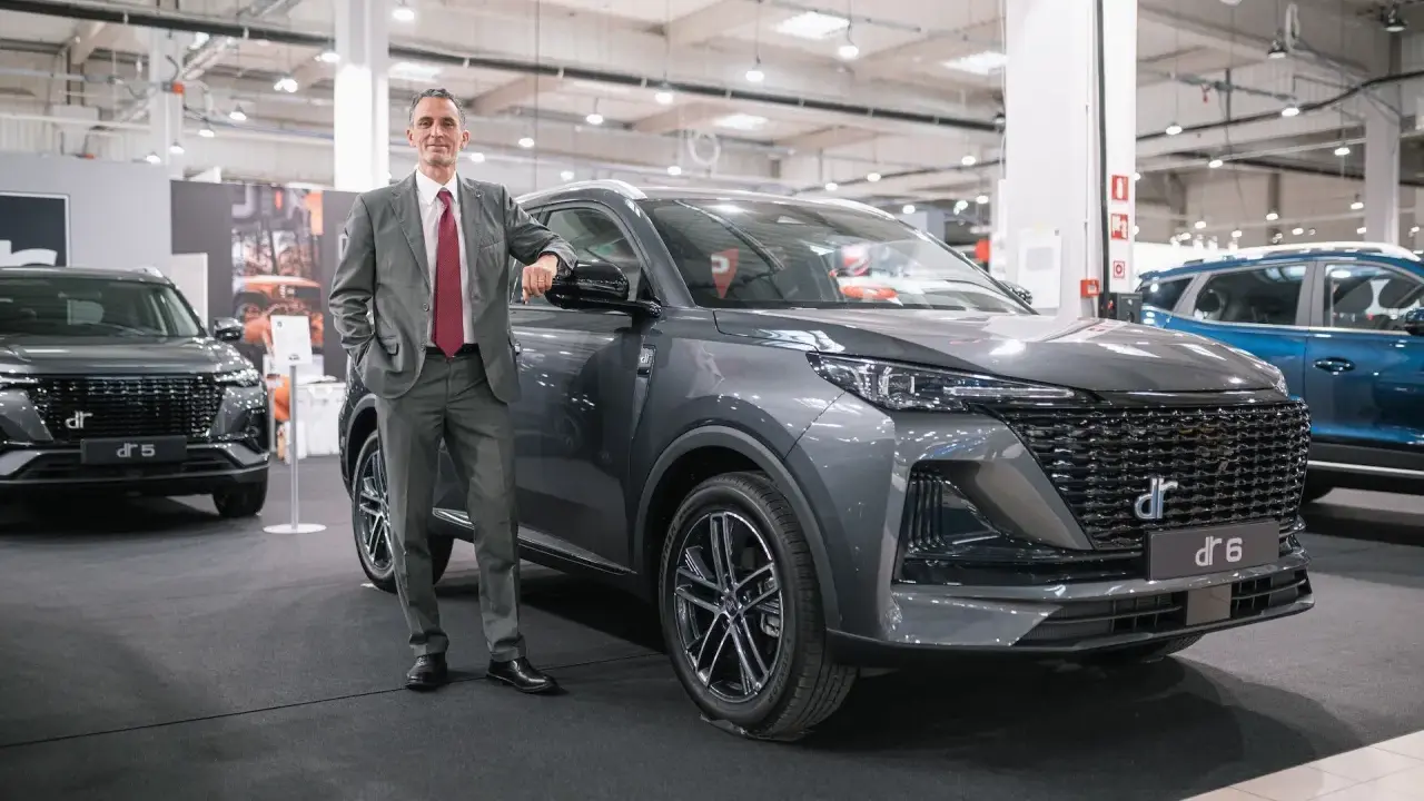 Mężczyzna w garniturze opiera się o szare auto DR 6. Obok stoi DR 5.