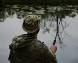 Wędkarz w kamuflażu przygotowuje się do łowienia. Pokazano, jak uzbroić wędkę na spinning, z przynętą gotową do zarzucenia.