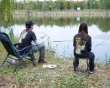 Para wędkująca nad jeziorem, w koszulkach z napisem "Lure Fishing". Cieszą się spokojem, choć ich hobby to czysta komercja.
