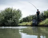 Wędkarz łowiący spinningiem na rzece, z podbierakiem i sprzętem wędkarskim.
