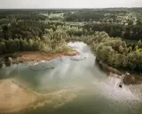Malownicze jezioro Świętajno otoczone lasami i trzcinami. W oddali widać zabudowania wsi.