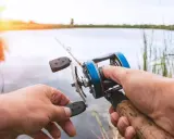 Ręce trzymające kołowrotek spinningowy. Długość wędki na spinning jest kluczowa dla komfortu łowienia.