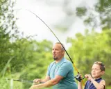 Ojciec i syn łowią ryby. Wędka wygięta w łuk, widać napięcie i skupienie podczas akcji wędki.