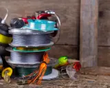 Stos szpul z żyłką i plecionką na spinning, obok kolorowe przynęty. Wybór między żyłką czy plecionką na spinning zależy od łowiska.