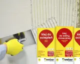 Ręka w żółtej rękawicy nakłada klej do ociepleń na ścianę. Obok worki z klejem do wełny mineralnej i do ociepleń.