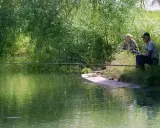 Dwaj wędkarze siedzą nad zieloną wodą. Różnica między castingiem a spinningiem jest subtelna, podobnie jak między tymi dwoma metodami łowienia.