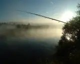 Wędka nad mglistą rzeką o wschodzie słońca.