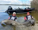 Dwóch wędkarzy z gigantycznym sumem, prawdopodobnie rekord polski sum. W tle łódź i elektrownia.