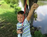 Chłopiec z wędką trzyma złowioną rybę nad wodą.
