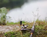 Wędka i kołowrotek leżą na trawie nad wodą, gotowe do połowu. Czas na tarło ryb!