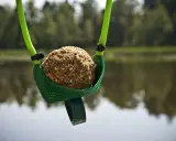 Zielona proca do zanęty z kulką zanętową gotowa do rzutu nad spokojną wodą.