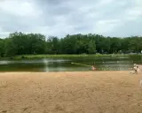 Piękna, piaszczysta plaża w Dziećkowicach zaprasza do wypoczynku nad jeziorem. W tle zielony las i spokojna woda.