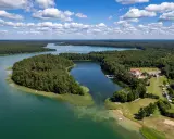 Malownicze jezioro Lechickie otoczone lasem, z hotelem i polem kempingowym na brzegu.