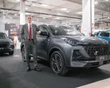 Mężczyzna w garniturze opiera się o szare auto DR 6. Obok stoi DR 5.
