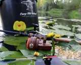 Wędka, kołowrotek i przynęta na karpia na tle stawu z liliami. Idealne miejsce, by dowiedzieć się, jak złowić karpia na spławik.