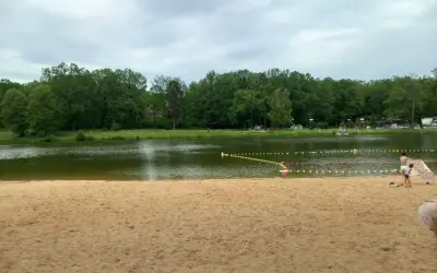 Piękna, piaszczysta plaża w Dziećkowicach zaprasza do wypoczynku nad jeziorem. W tle zielony las i spokojna woda.