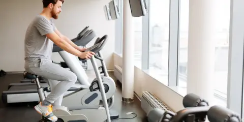 Mężczyzna ćwiczy na rowerze stacjonarnym w siłowni.