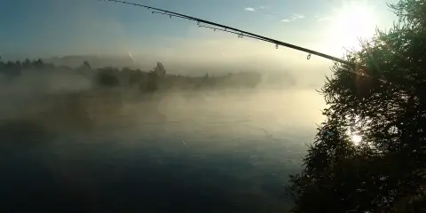 Wędka nad mglistą rzeką o wschodzie słońca.