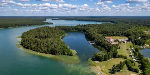 Malownicze jezioro Lechickie otoczone lasem, z hotelem i polem kempingowym na brzegu.