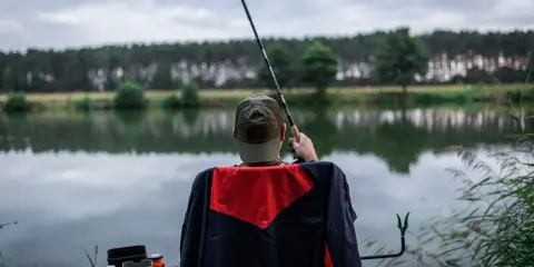 Wędkarz z klasycznym feederem czeka na branie nad spokojnym jeziorem. Jaka wędka do klasycznego feedera? Ta wydaje się idealna.