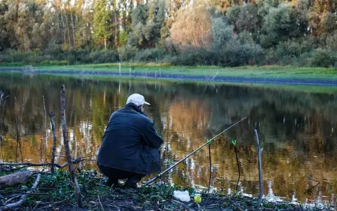 Wędkarz siedzi nad jeziorem, czekając na branie. Na brzegu leży zanęta na tołpyge, gotowa do użycia.