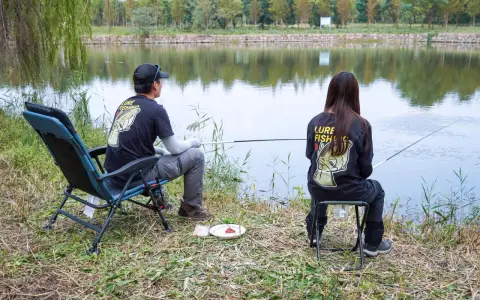 Para wędkująca nad jeziorem, w koszulkach z napisem "Lure Fishing". Cieszą się spokojem, choć ich hobby to czysta komercja.