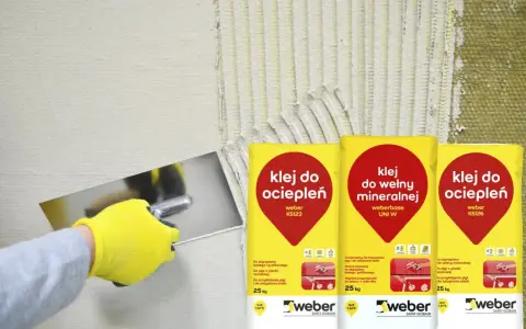 Ręka w żółtej rękawicy nakłada klej do ociepleń na ścianę. Obok worki z klejem do wełny mineralnej i do ociepleń.