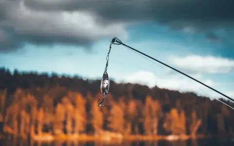 Przynęta z haczykiem wisi na żyłce, gotowa do połowu na jeziorze Skarlińskim. W tle jesienne drzewa i błękitne niebo.
