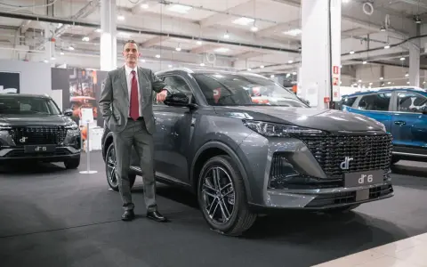 Mężczyzna w garniturze opiera się o szare auto DR 6. Obok stoi DR 5.