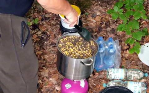 Przygotowanie grochu na ryby: duży garnek z ziarnami kukurydzy i grochu na kuchence turystycznej. W tle butelki z wodą.