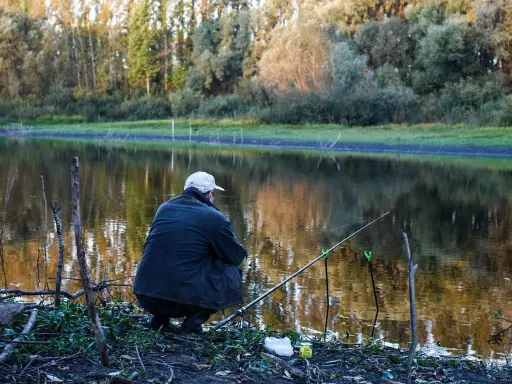 Wędkarz siedzi nad jeziorem, czekając na branie. Na brzegu leży zanęta na tołpyge, gotowa do użycia.