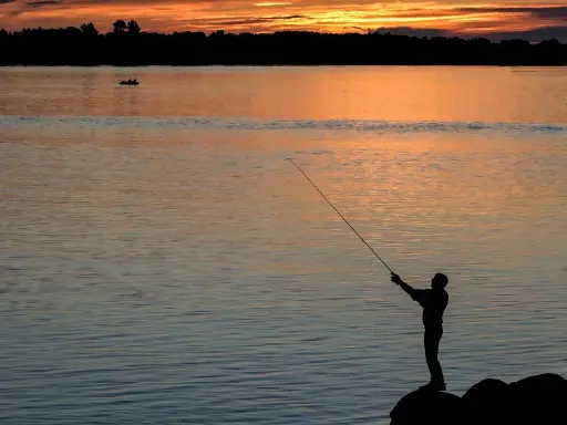 Sylwetka wędkarza łowiącego ryby o zachodzie słońca nad jeziorem.