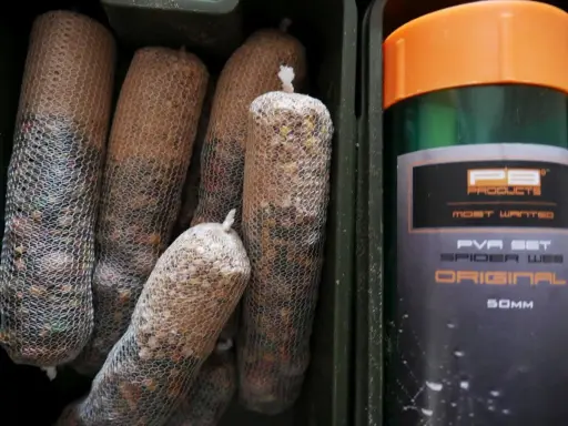 Wędkarskie stiki w siatkach PVA, gotowe do użycia. Obok zielony pojemnik z pomarańczową nakrętką.