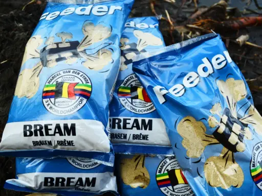 Kilka opakowań zanęt na leszcza "Feeder" z wizerunkiem belgijskiej flagi i napisem "3 x World Champion".