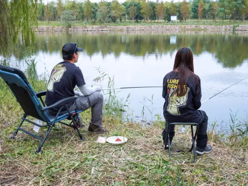 Para wędkująca nad jeziorem, w koszulkach z napisem "Lure Fishing". Cieszą się spokojem, choć ich hobby to czysta komercja.