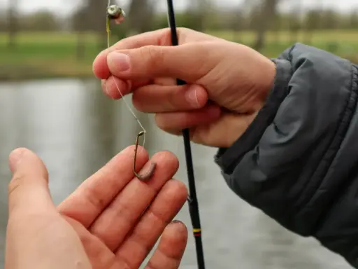 Dłonie wędkarza zakładają robaka na haczyk nad wodą.