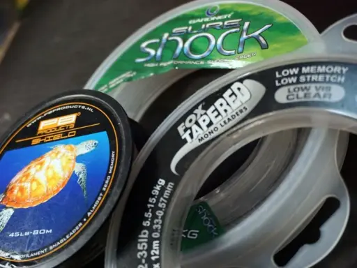 Wybór między żyłką a plecionką to kluczowa decyzja wędkarza. Na zdjęciu widać różne rodzaje żyłek, w tym PB Products Shield i Fox Tapered Mono Leaders.