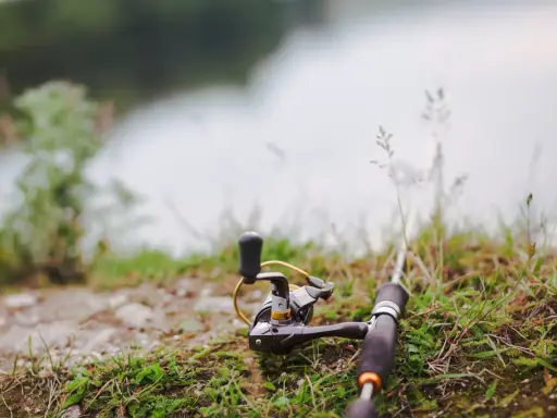 Wędka i kołowrotek leżą na trawie nad wodą, gotowe do połowu. Czas na tarło ryb!