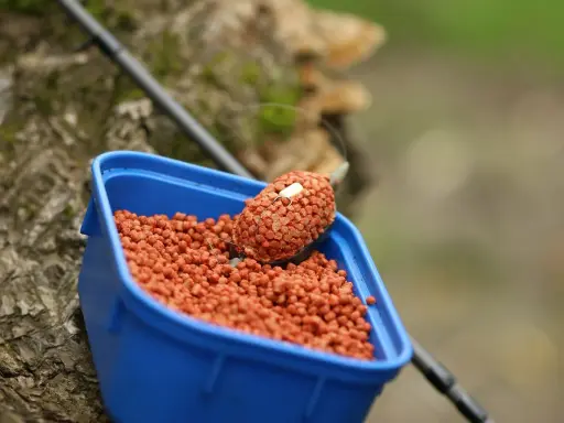 Niebieskie pudełko z zanętami Lorpio feeder, gotowe do akcji. Wędka w tle.