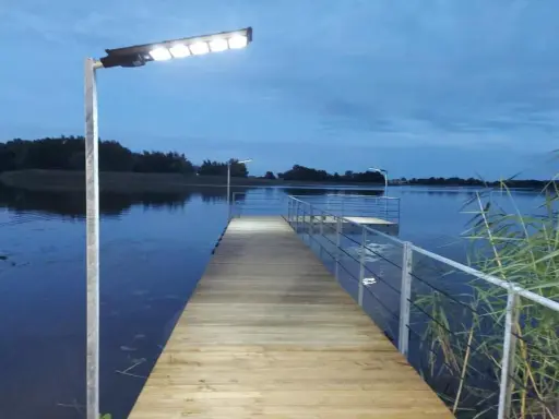 Drewniany pomost nad jeziorem, oświetlony lampami, zachęca do spaceru. Czy pomost nad jeziorem może być prywatny? Ten wygląda na dostępny dla wszystkich.