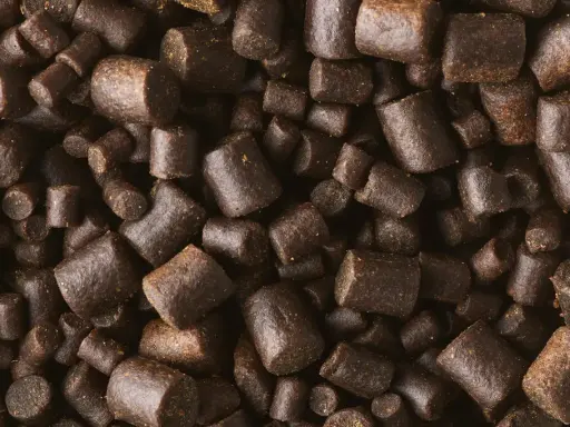 Zbliżenie na ciemnobrązowe granulki, które mogą być składnikiem zanęty na karpia jak zrobić.