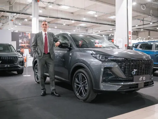 Mężczyzna w garniturze opiera się o szare auto DR 6. Obok stoi DR 5.