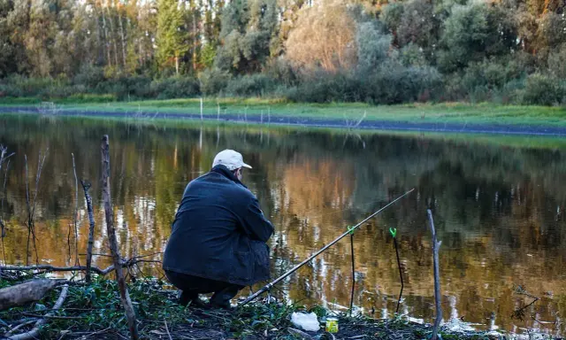 Wędkarz siedzi nad jeziorem, czekając na branie. Na brzegu leży zanęta na tołpyge, gotowa do użycia.