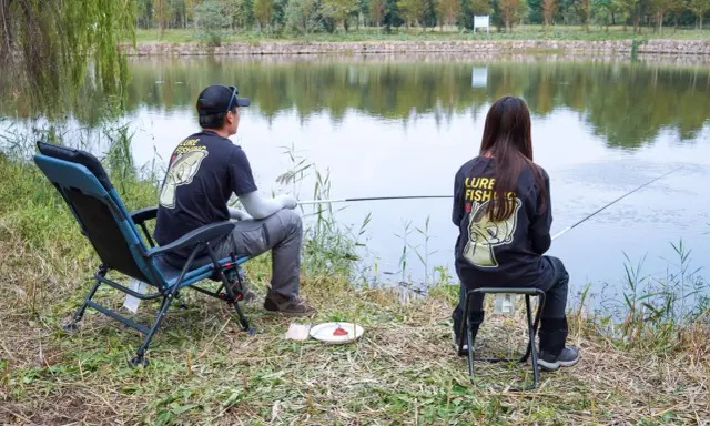 Para wędkująca nad jeziorem, w koszulkach z napisem "Lure Fishing". Cieszą się spokojem, choć ich hobby to czysta komercja.