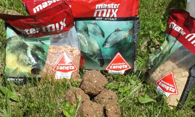 Kilka opakowań zanęta wędkarska 10kg i kulki proteinowe na trawie.