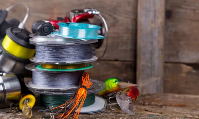 Stos szpul z żyłką i plecionką na spinning, obok kolorowe przynęty. Wybór między żyłką czy plecionką na spinning zależy od łowiska.