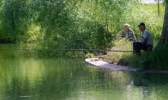 Dwaj wędkarze siedzą nad zieloną wodą. Różnica między castingiem a spinningiem jest subtelna, podobnie jak między tymi dwoma metodami łowienia.
